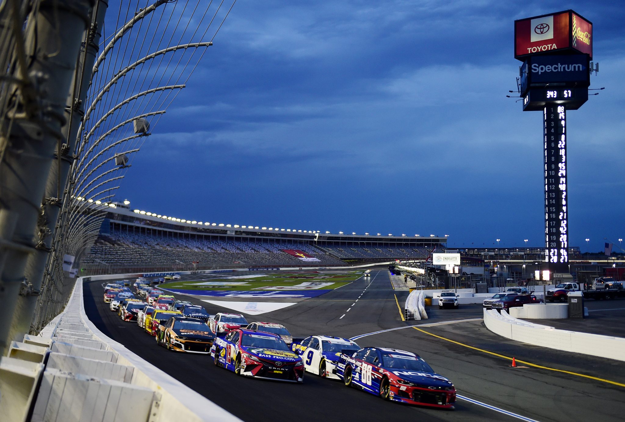 Cup Series cars racing into the night at Charlotte Motor Speedway under the lights
