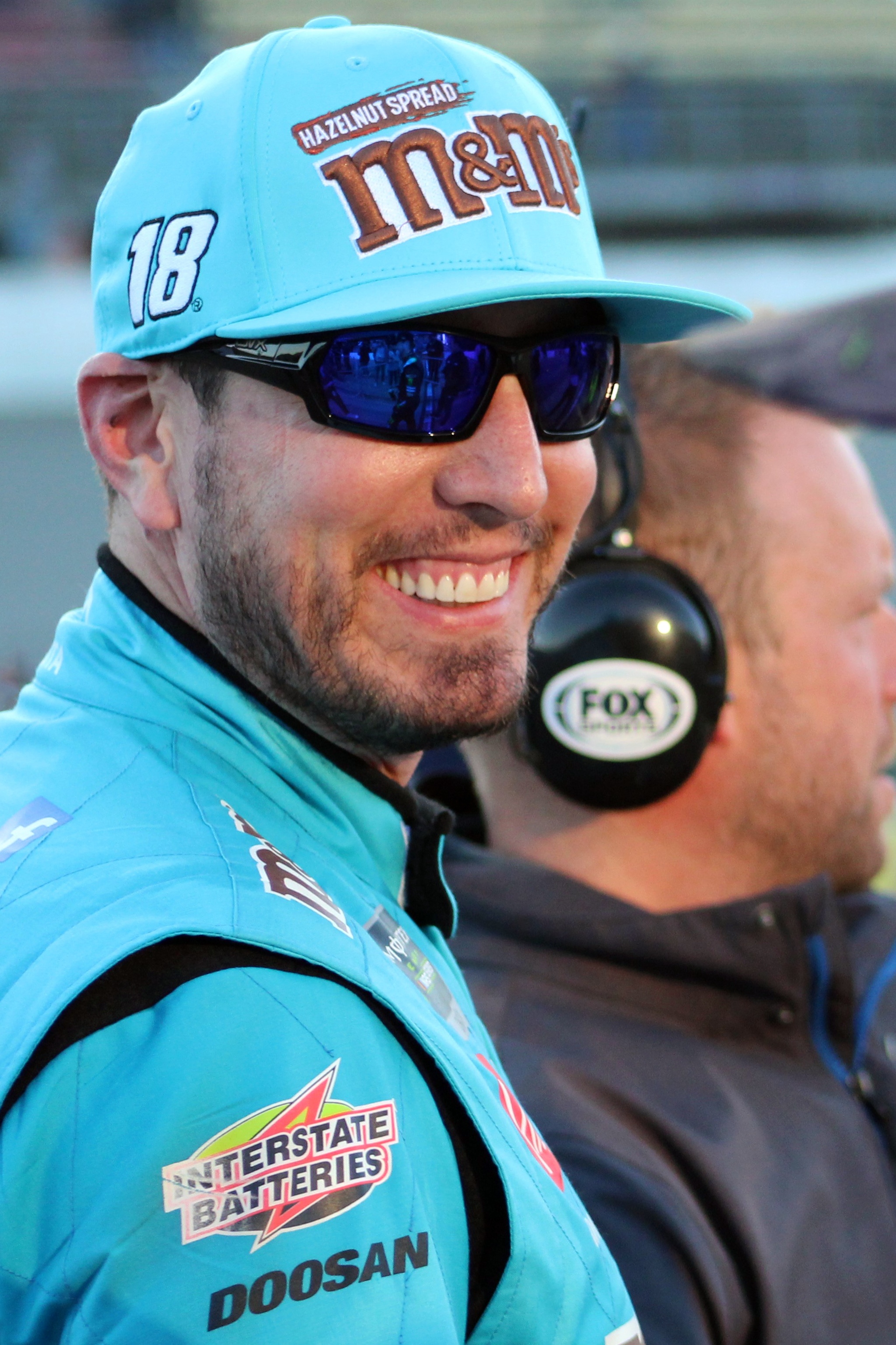 Kyle Busch grinning in his No. 18 M&M's cap and firesuit