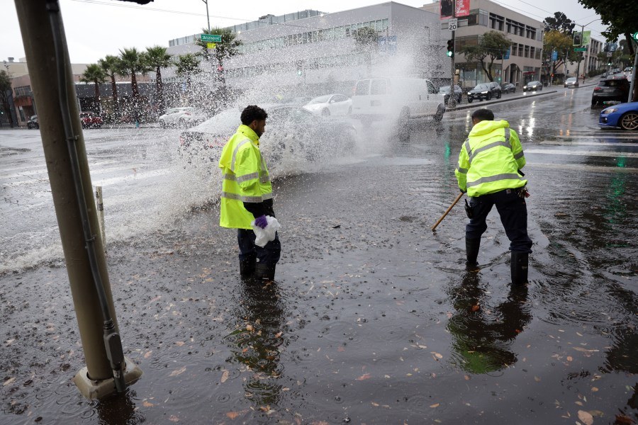 City workers in reflective jackets clear standing water from a flooded Southern California intersection during a recent storm