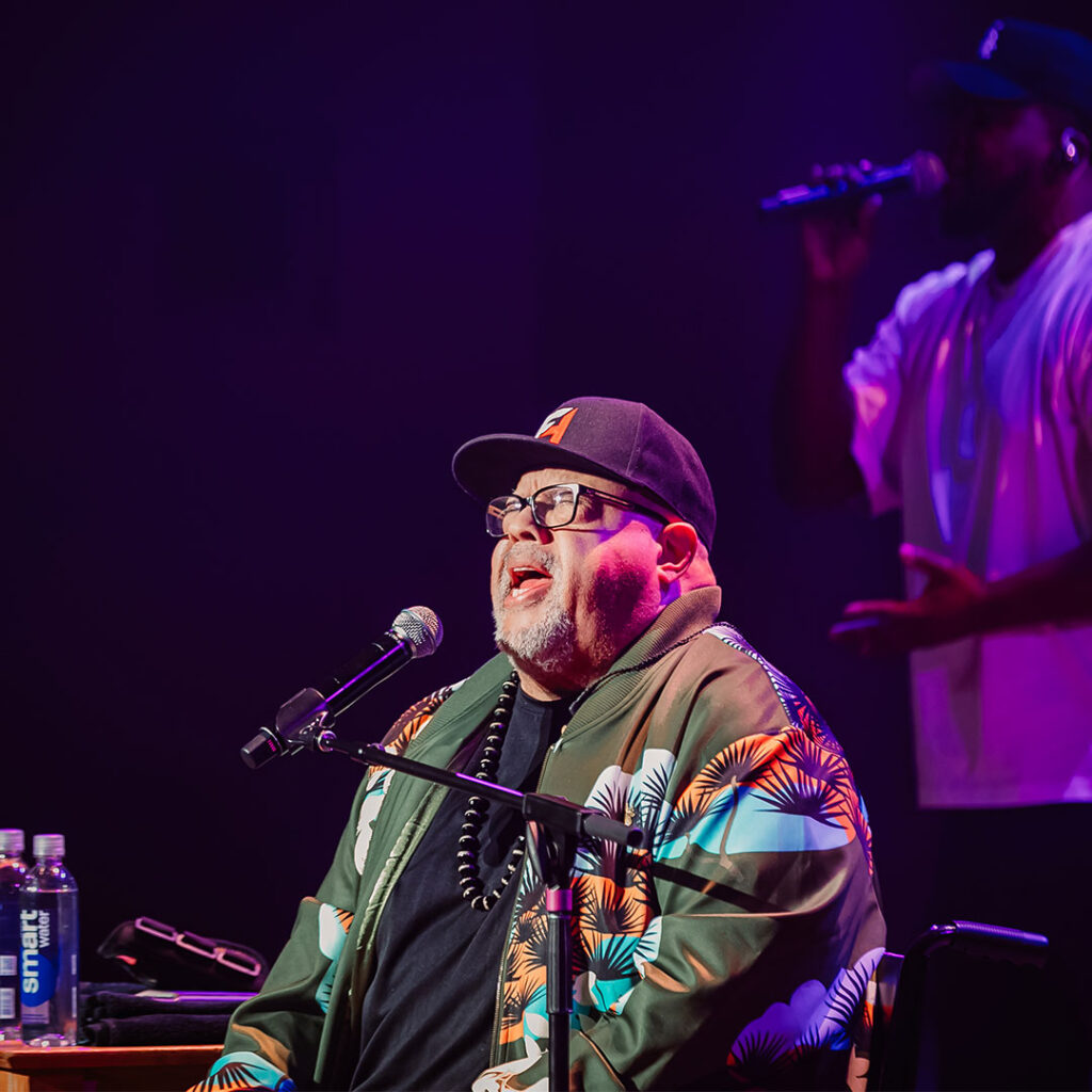Fred Hammond performing on stage in a colorful jacket