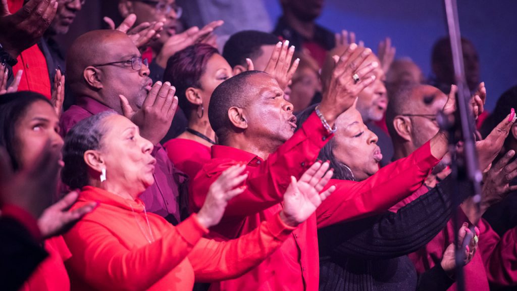 A gospel choir in red with hands raised in worship