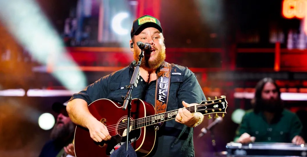 Luke Combs performing on stage with his acoustic guitar in front of a live crowd