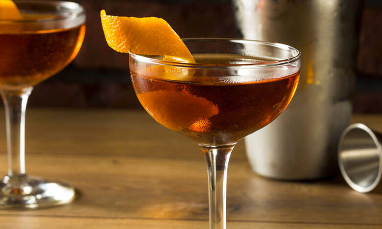 A Martinez cocktail in a coupe glass with an orange peel garnish — the amber drink that bridged the Manhattan and the Martini