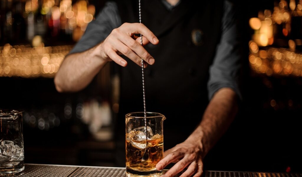 A bartender stirring a cocktail in a mixing glass with a bar spoon — the Martinez is always stirred, never shaken