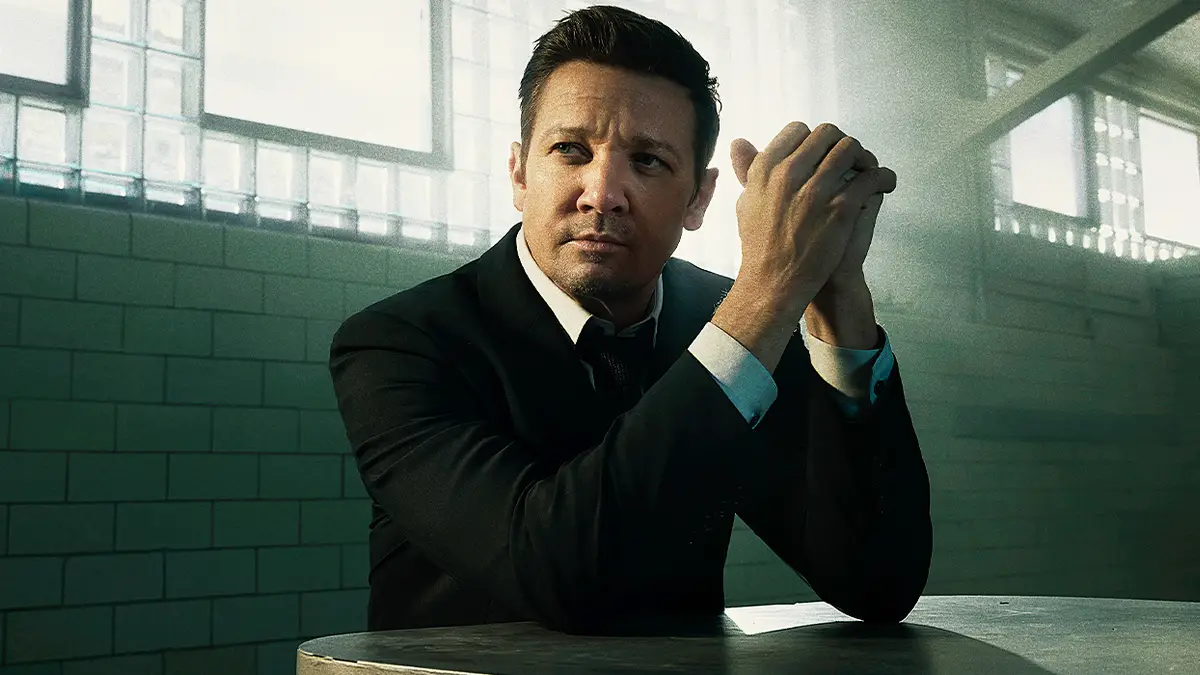 Jeremy Renner as Mike McLusky in 'Mayor of Kingstown', seated in a suit in a prison visitation room