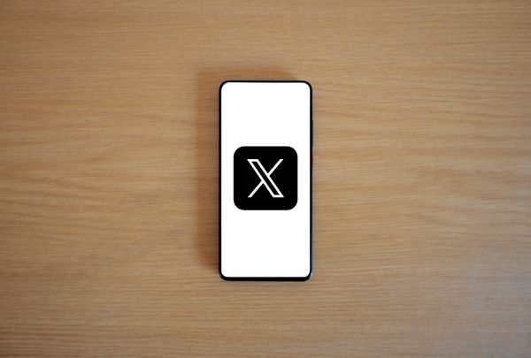 A smartphone displaying the X logo on a wooden table