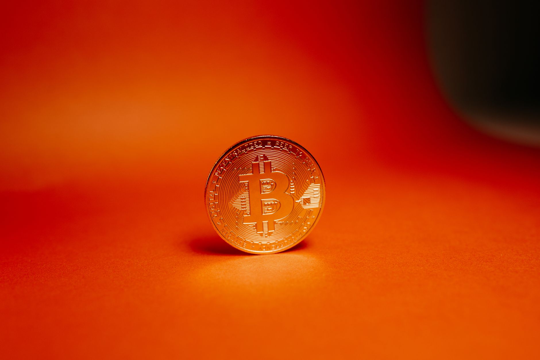 A physical Bitcoin coin photographed on a warm orange background