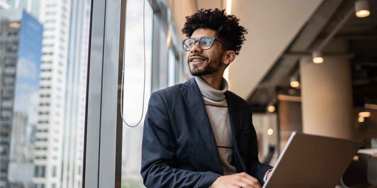 A professional holding a laptop in a bright modern office with large windows