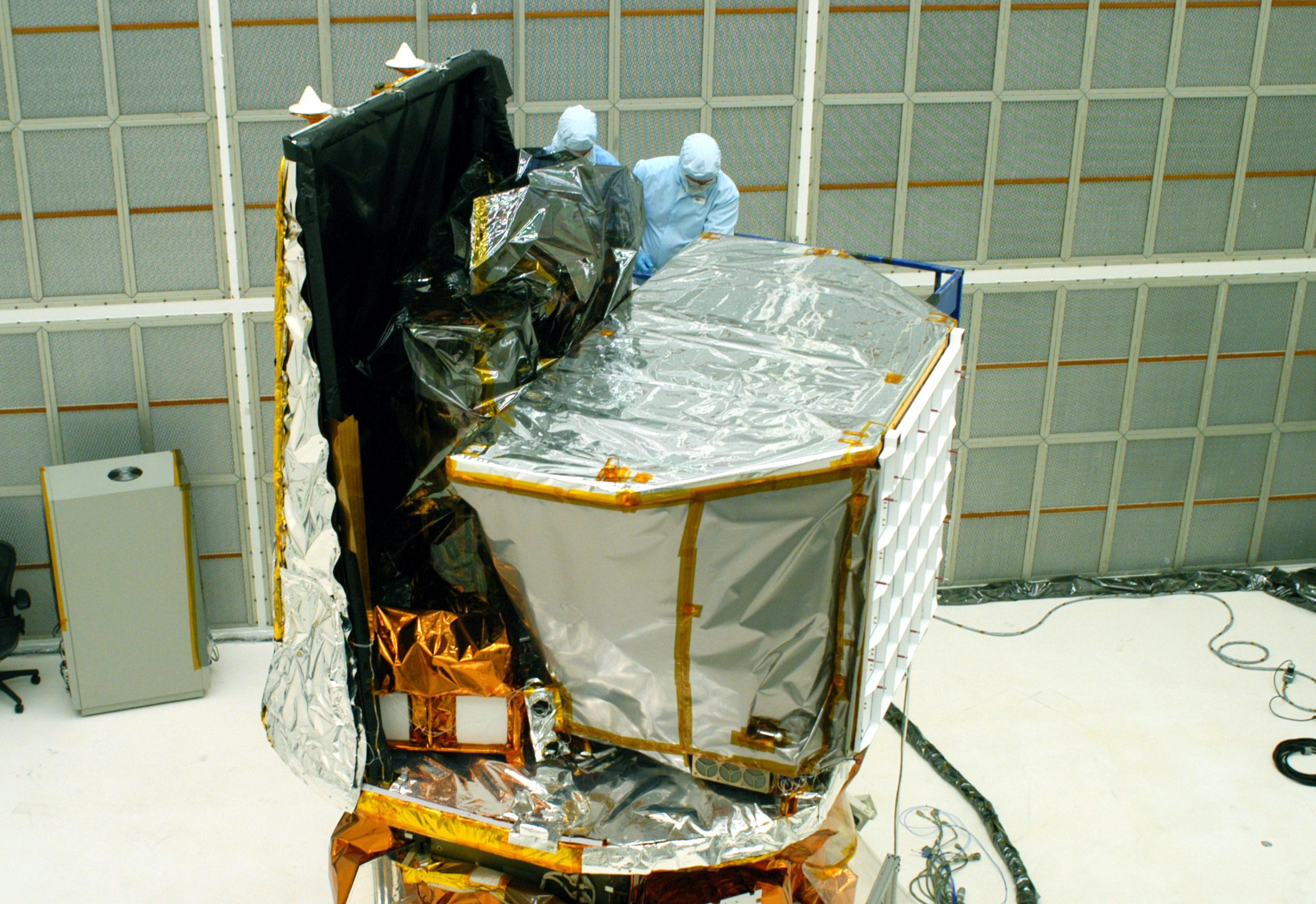 The Swift spacecraft in a clean room at Cape Canaveral in 2004, technicians in protective suits removing its final covers before launch
