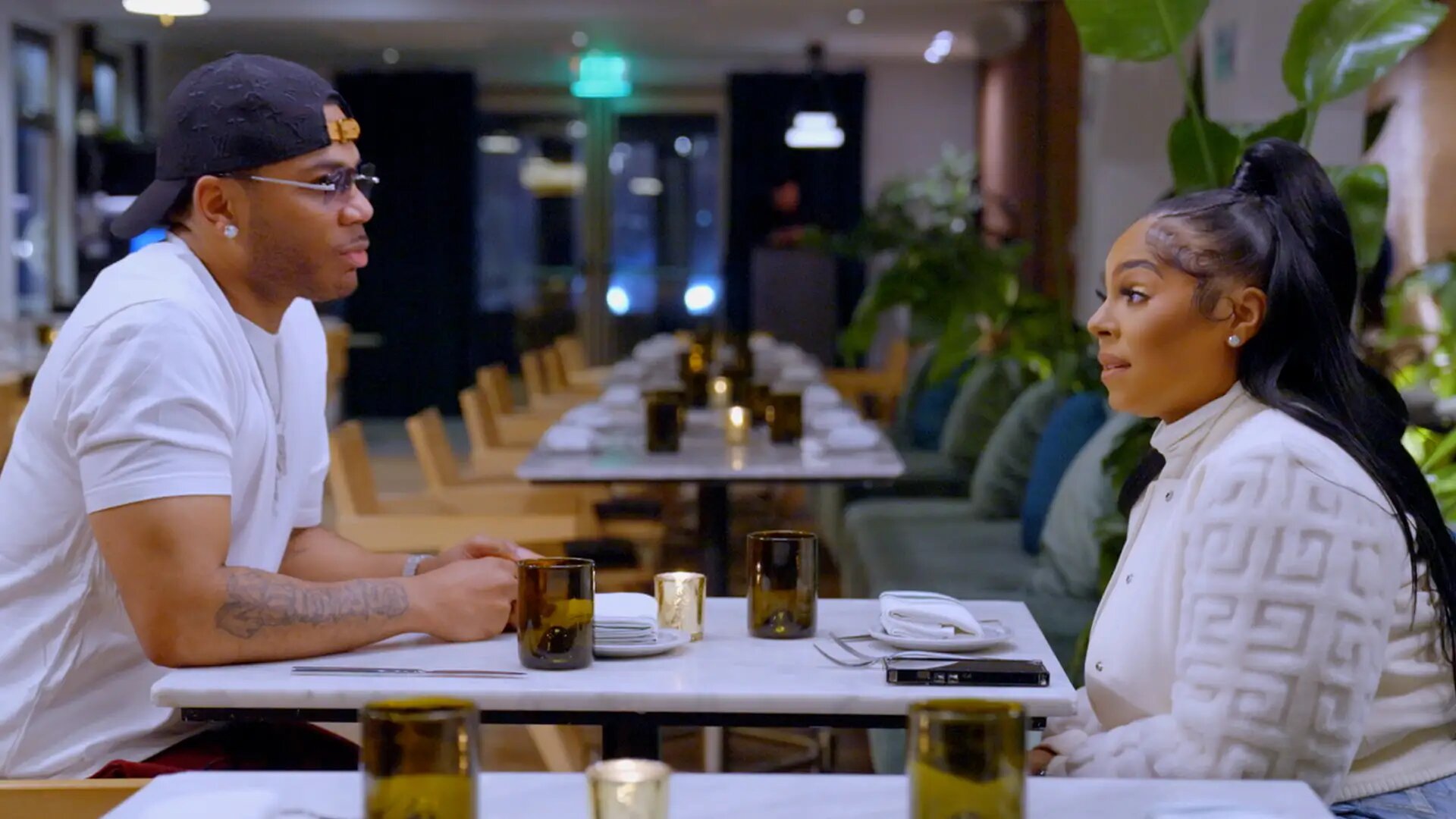 Nelly and Ashanti face-to-face across a restaurant table, from Season 1 of Nelly & Ashanti: We Belong Together