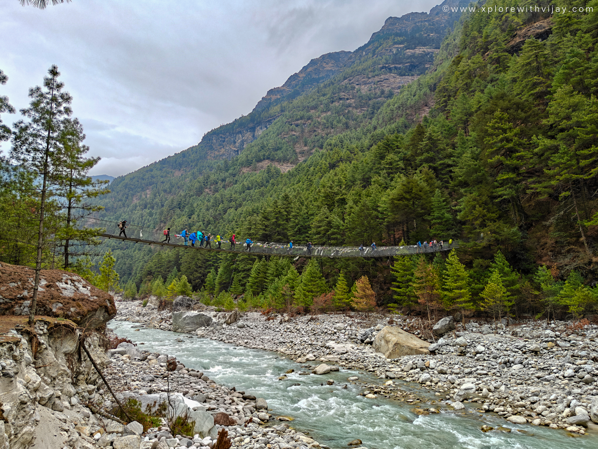 Trekkers crossing a suspension bridge over a Himalayan river in Nepal