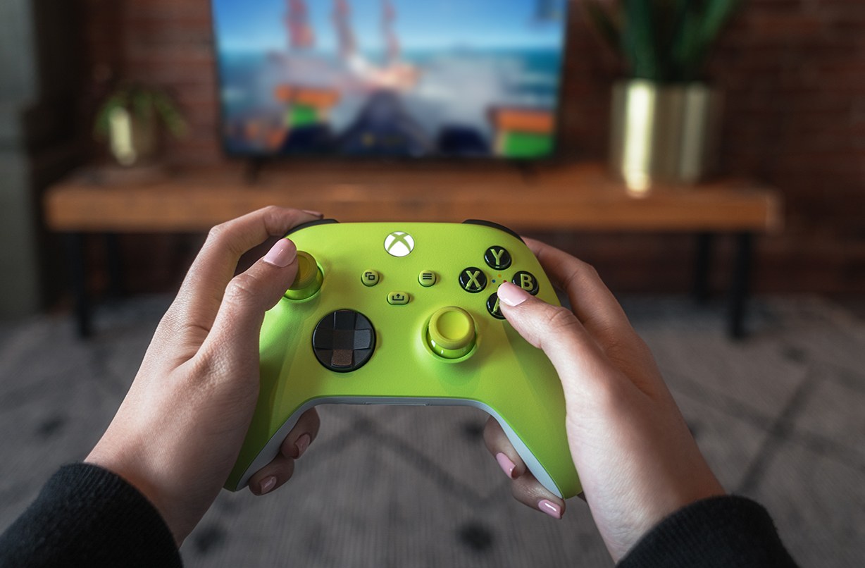 Hands holding a lime-green Xbox controller in front of a TV