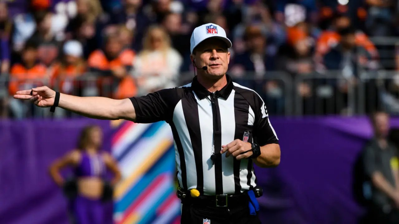 An NFL referee in stripes signaling a call on the field during a game.