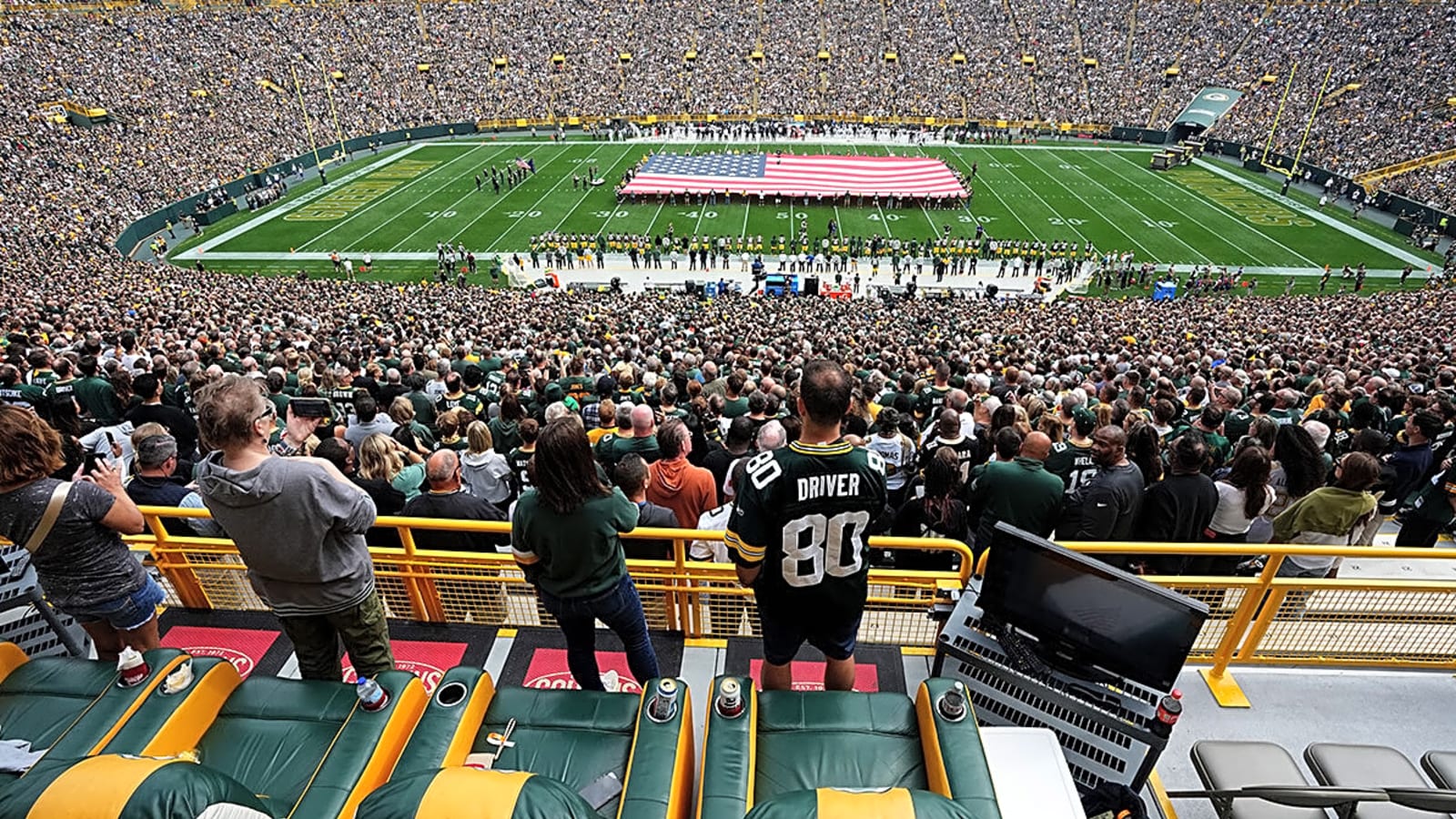 Green Bay Packers fans pack Lambeau Field for pregame festivities with a giant American flag on the field.