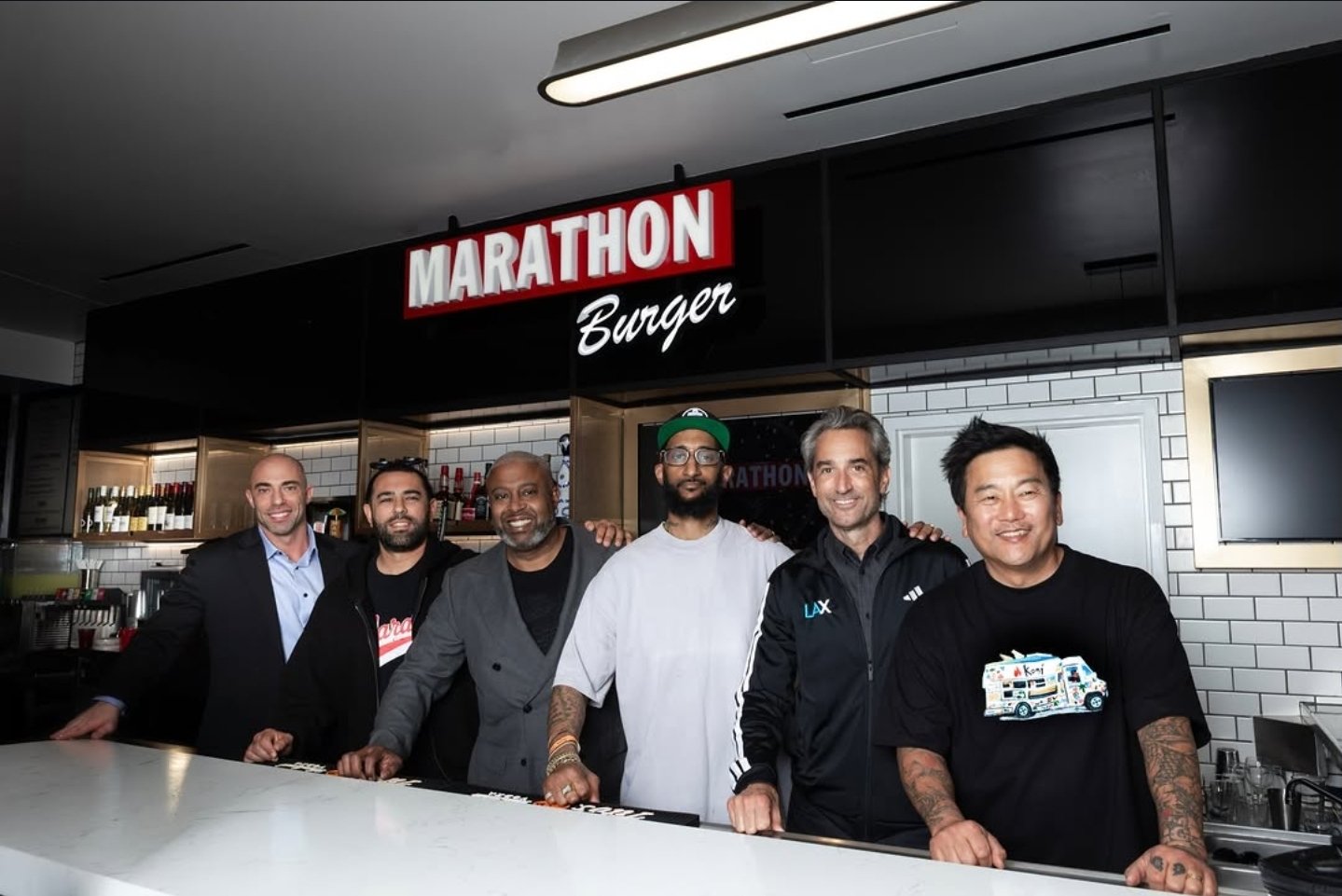 The Marathon Burger opening crew behind the counter at LAX Terminal 1, under the red Marathon Burger sign — Samiel “Blacc Sam” Asghedom in the green cap at center, with Roy Choi at the right