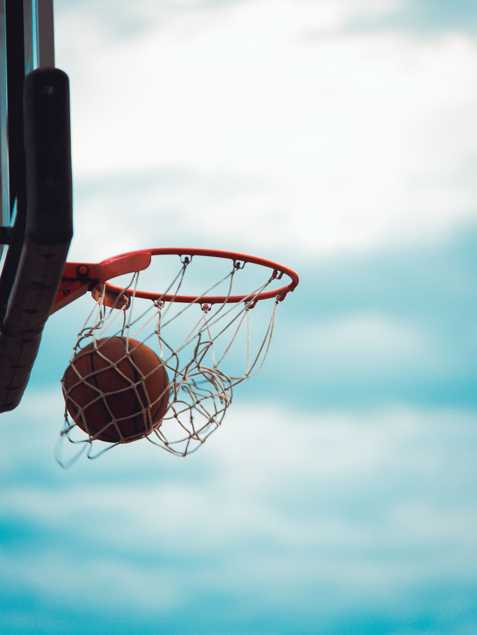 A basketball sinking through a hoop outdoors on a clear day (file photo)