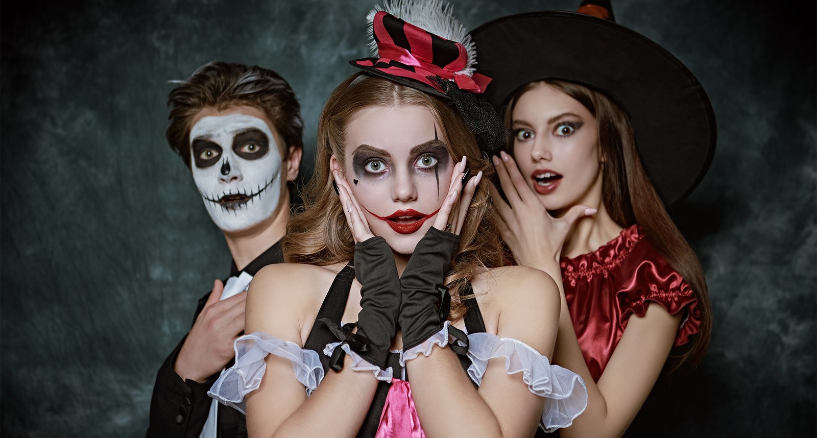 Three people in Halloween costumes — skeleton, harlequin and witch — posing in a studio