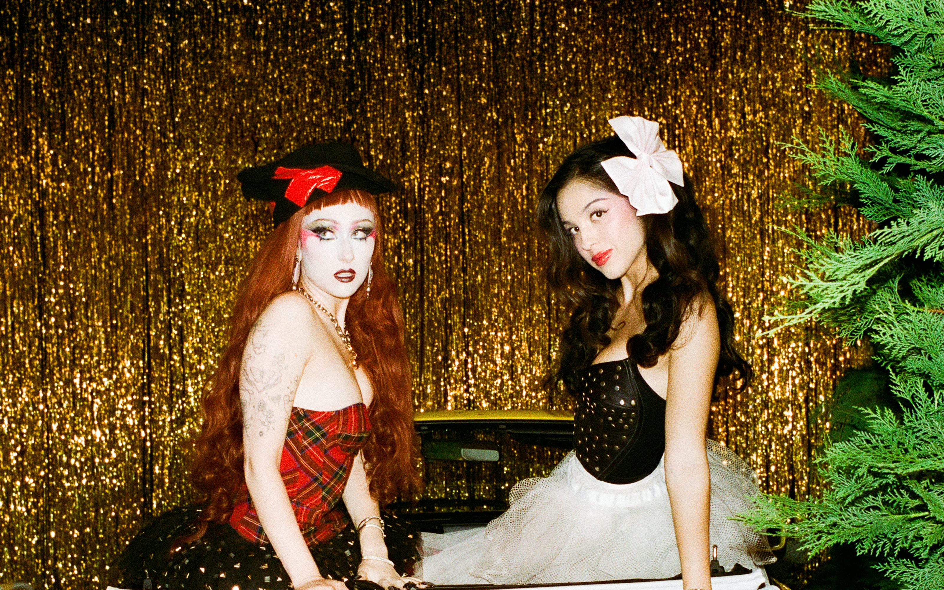 Olivia Rodrigo and Chappell Roan in 1980s-style outfits atop a vintage car on the set of the expectations remix video