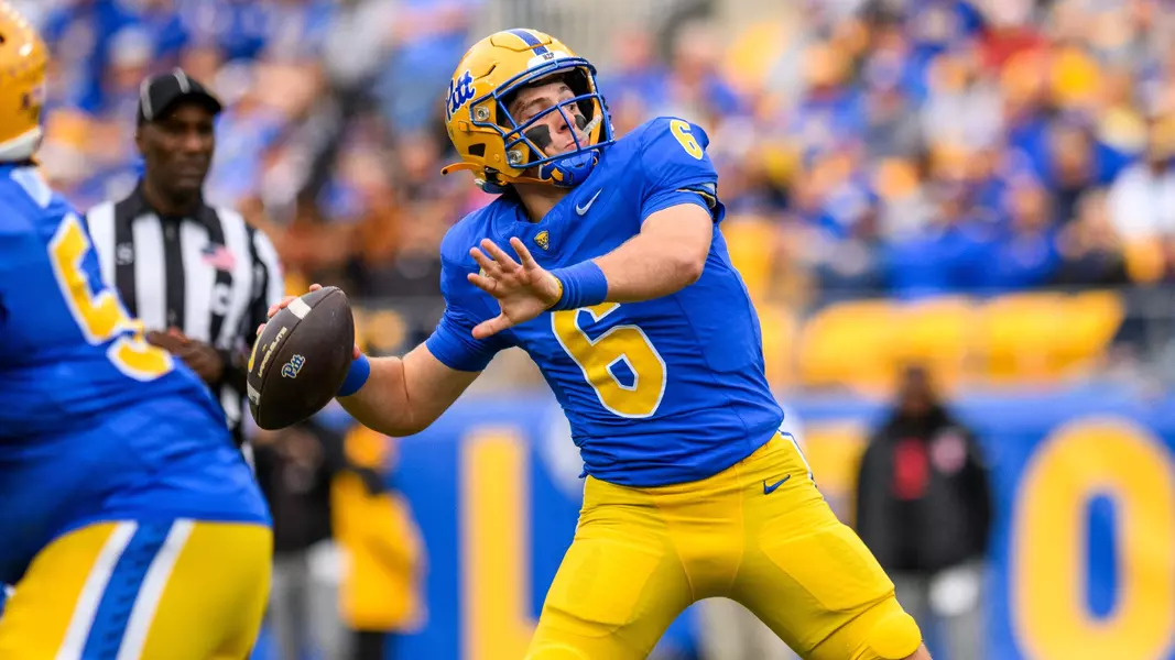 Pitt quarterback Mason Heintschel throwing in a daylight home game, navy blue and gold uniform