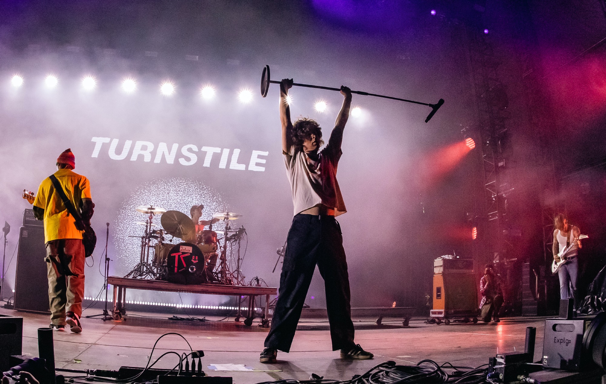 Turnstile performing live, singer holding a microphone stand aloft with the band name on the backdrop