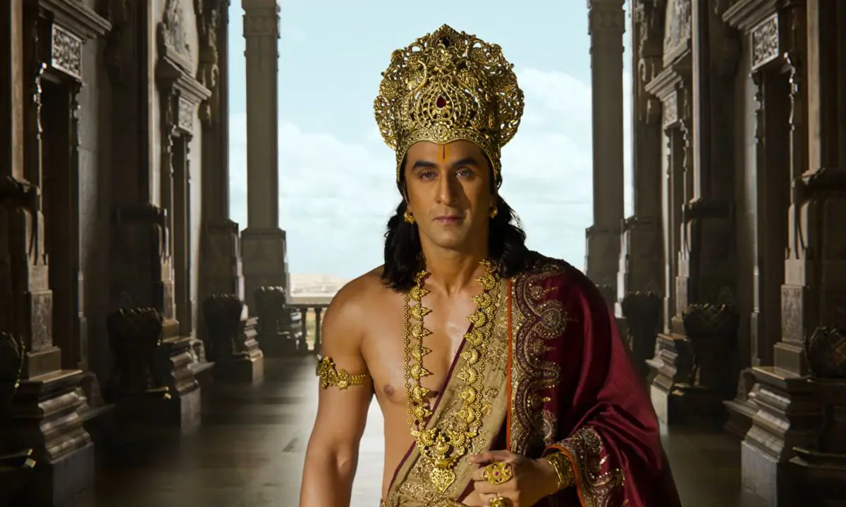 Ranbir Kapoor as Lord Rama in a palace corridor, wearing a golden crown and royal jewelry