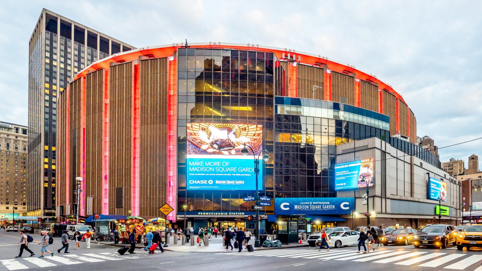 Madison Square Garden in Midtown Manhattan at dusk — the round arena lit in orange above its Chase entrance, with Pennsylvania Station below — 2019 file photo