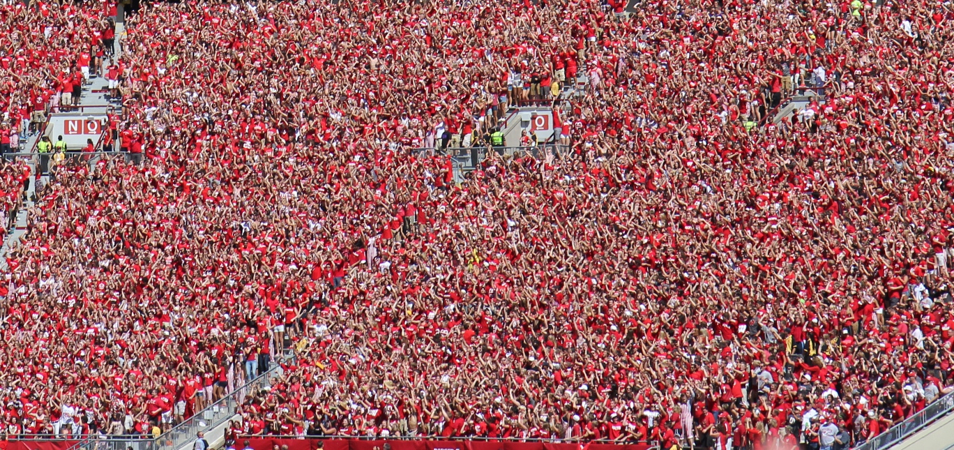 A sea of Wisconsin fans in red at Camp Randall Stadium, arms raised during the 'Jump Around' tradition — 2014 file photo