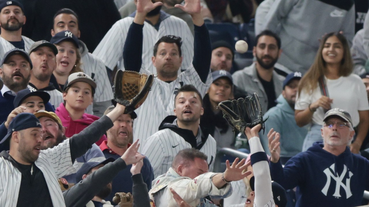 A Yankees fan reaches over the left-field fence into the field of play as the ball sails near the outfielder’s glove during ALDS Game 3 at Yankee Stadium