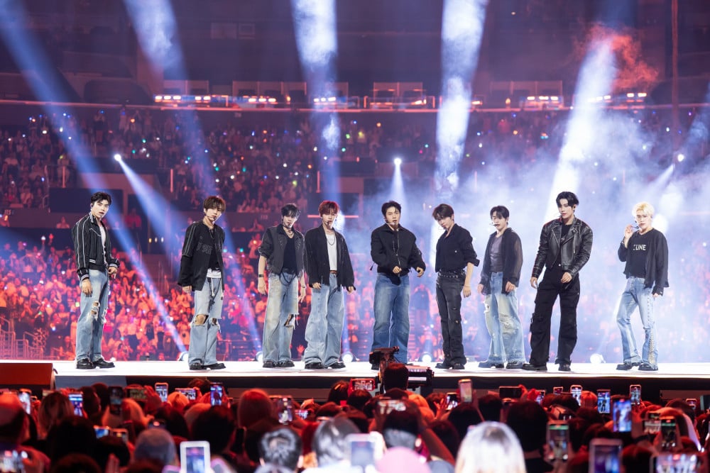 A K-pop boy group performing on a concert stage under bright lights