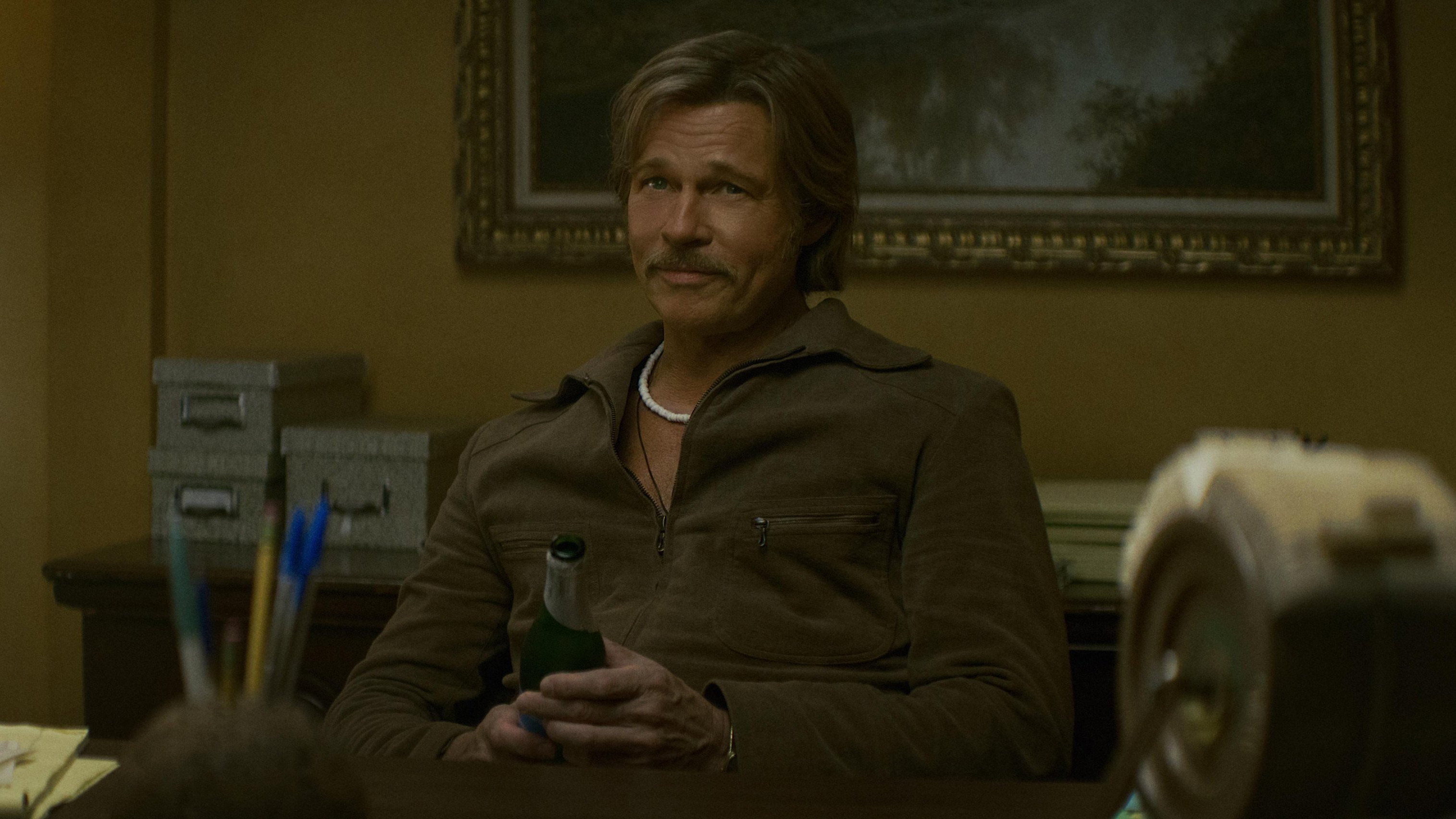 Brad Pitt as Cliff Booth in 'The Further Mis-Adventures of Cliff Booth' — the 1977 fixer at a desk, bottle in hand (Netflix still via TMDB)