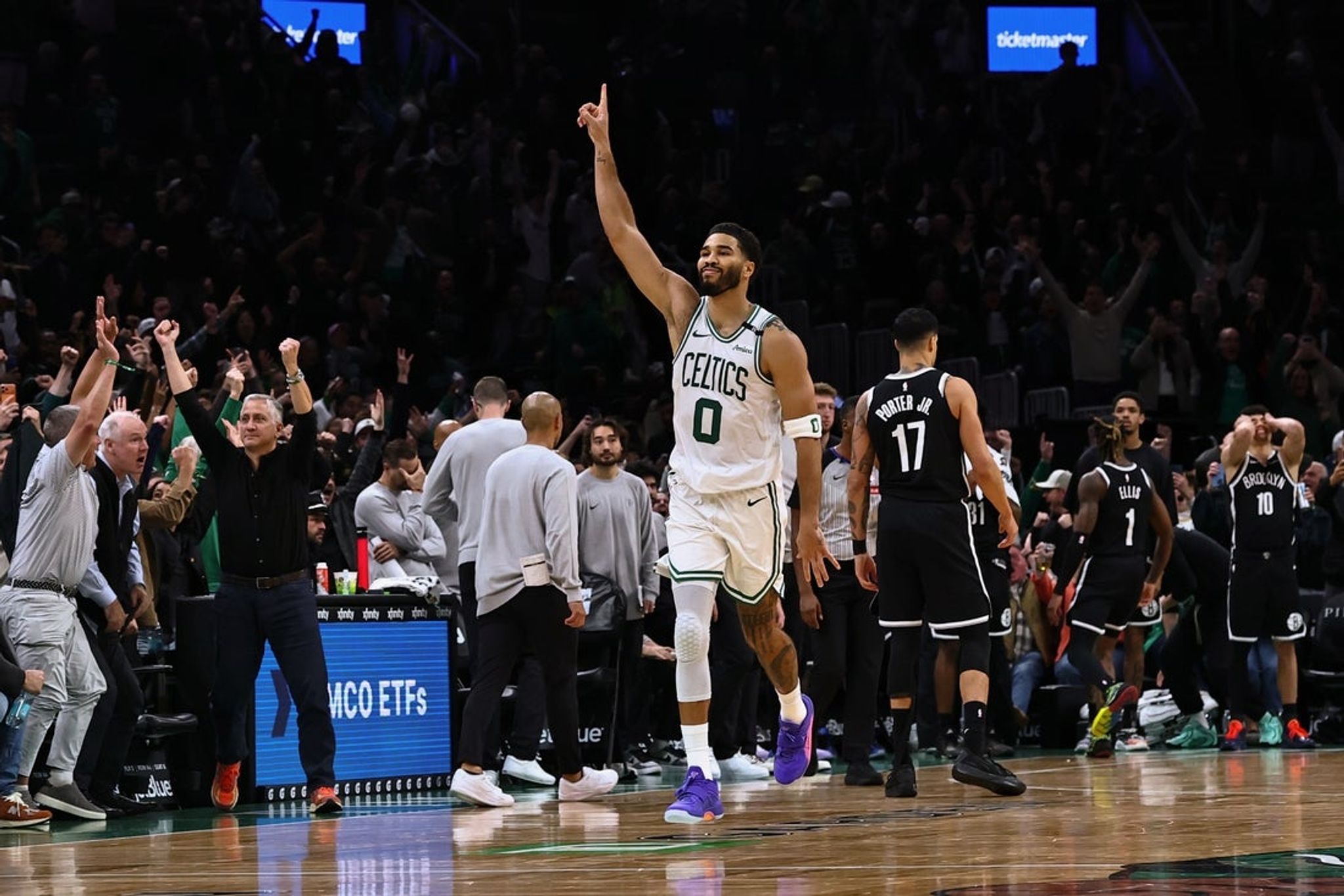 Jayson Tatum (Celtics white No. 0) celebrating his overtime game-winning shot at TD Garden, finger raised, with Michael Porter Jr. (Nets No. 17) in the foreground and the crowd erupting behind him
