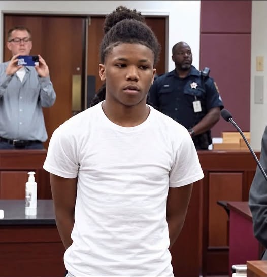 Anthony Rivers III, 15, stands in a Leon County courtroom at his detention hearing on Monday, in a white t-shirt with his hands behind his back and a uniformed officer behind him