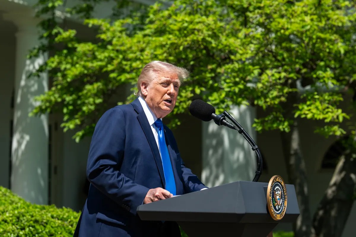 President Donald Trump speaking at a podium outside the White House on a bright day.
