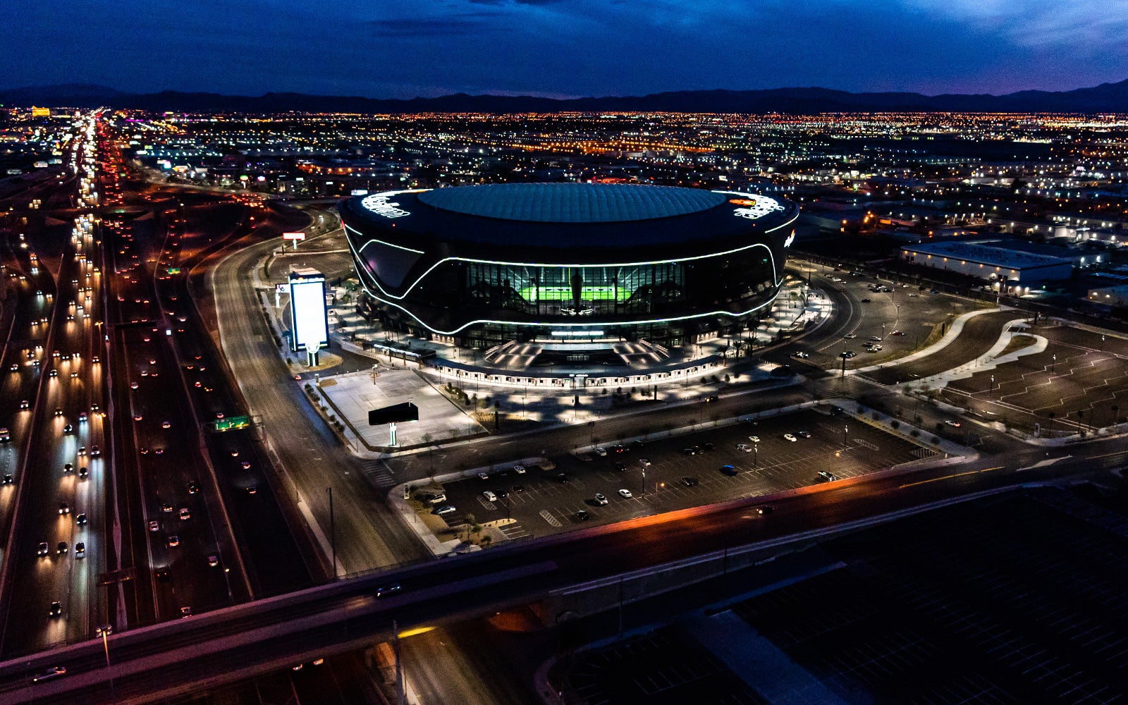 Allegiant Stadium lit up at night with I-15 traffic streaming past — a Saturday night in Las Vegas
