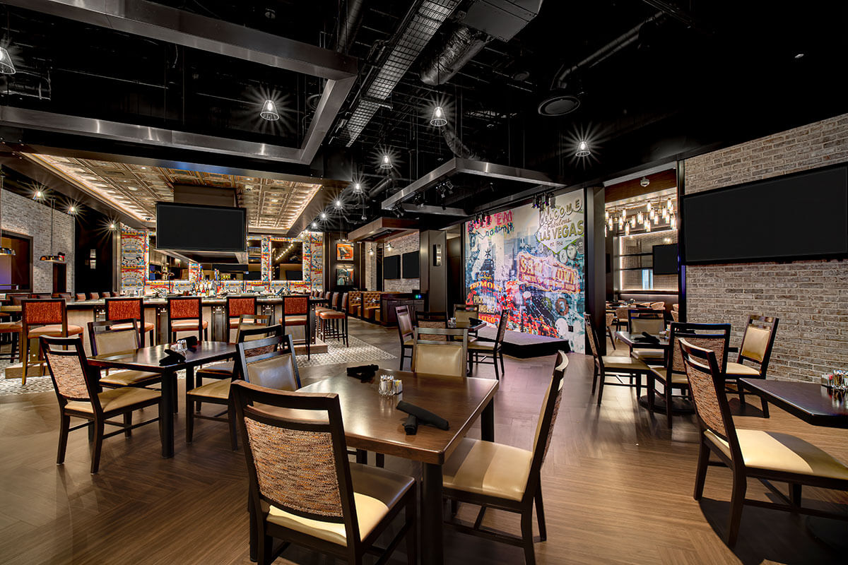 The dining room at Render Modern Kitchen inside Aliante Casino in North Las Vegas — central bar, performance stage and a Las Vegas mural wall
