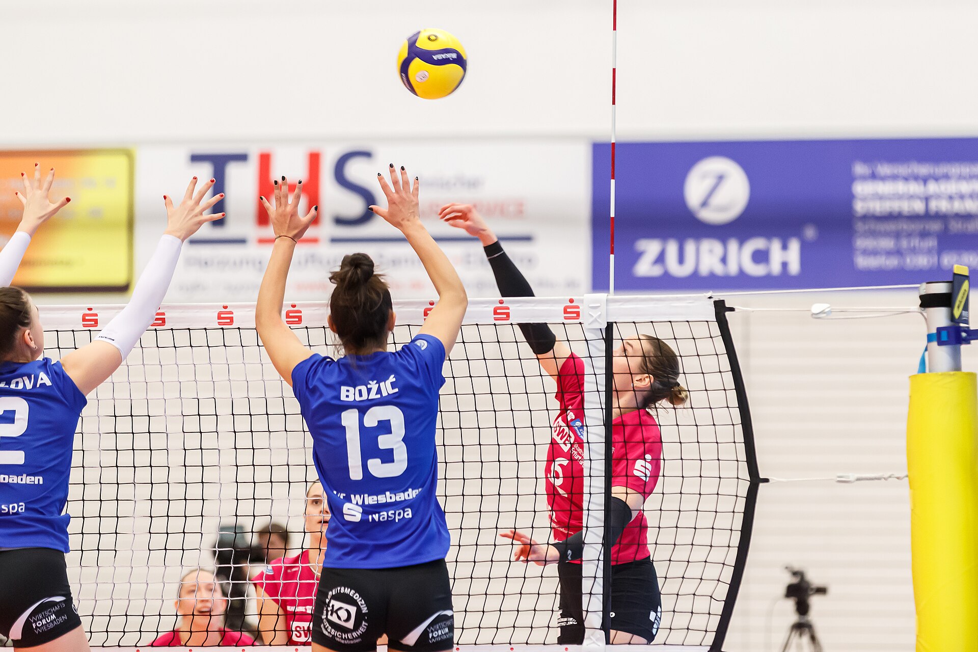 Two women's volleyball players jumping for a block at the net as an attacker swings