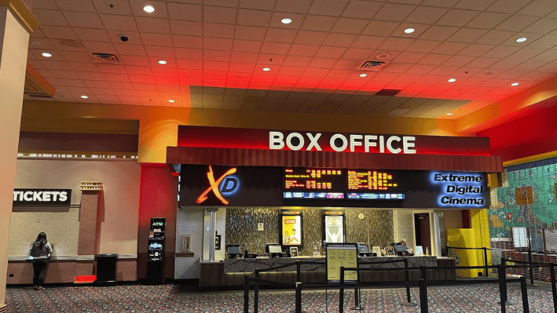 A cinema box office counter with lit signage over the ticket windows