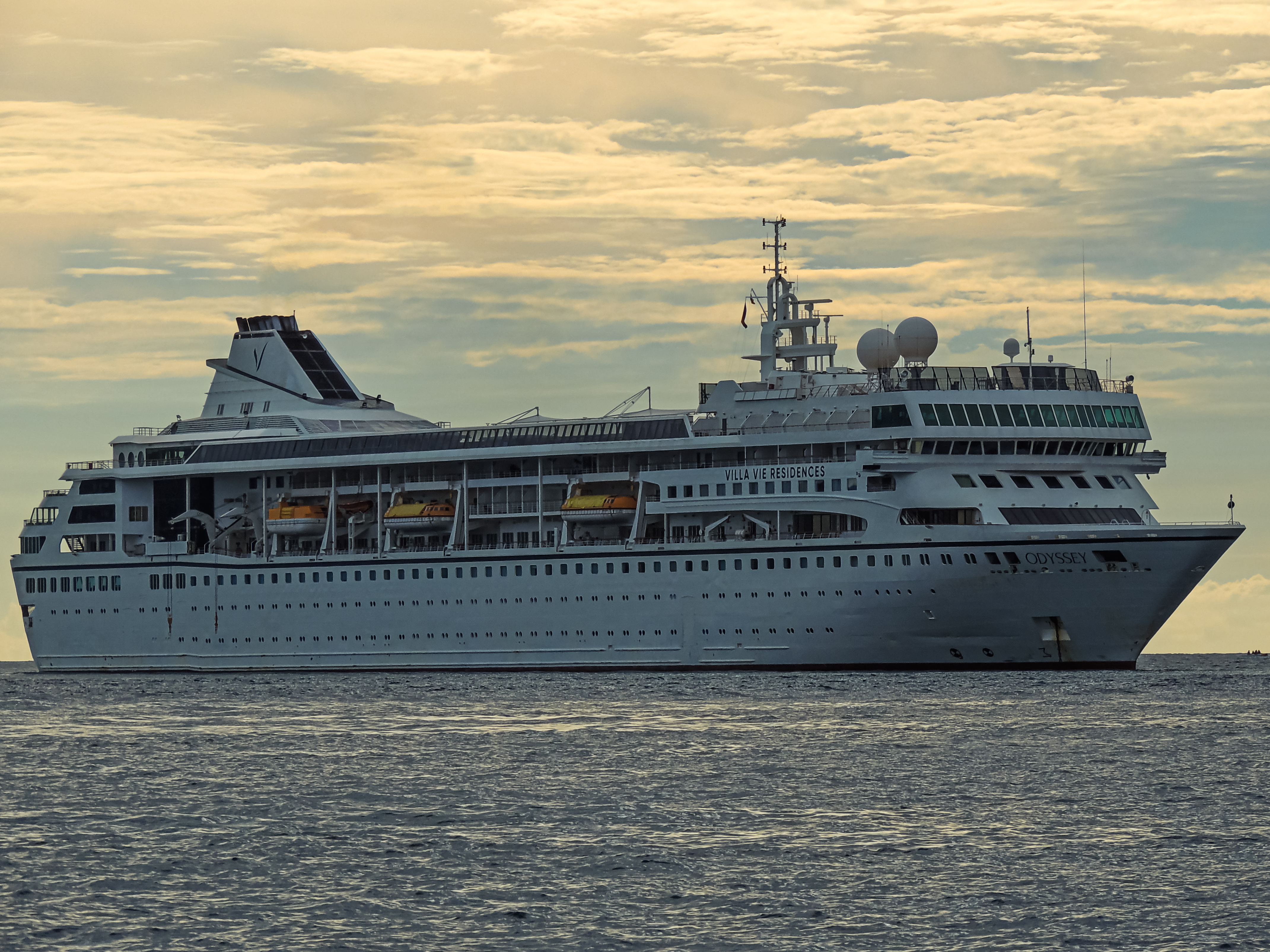 The Villa Vie Odyssey in her Villa Vie Residences livery at sea at golden hour, her name on the bow and Villa Vie Residences on the superstructure