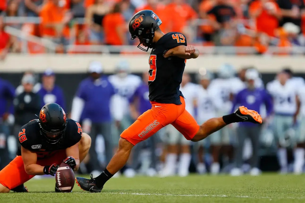 A college kicker striking a field goal attempt with the holder in place