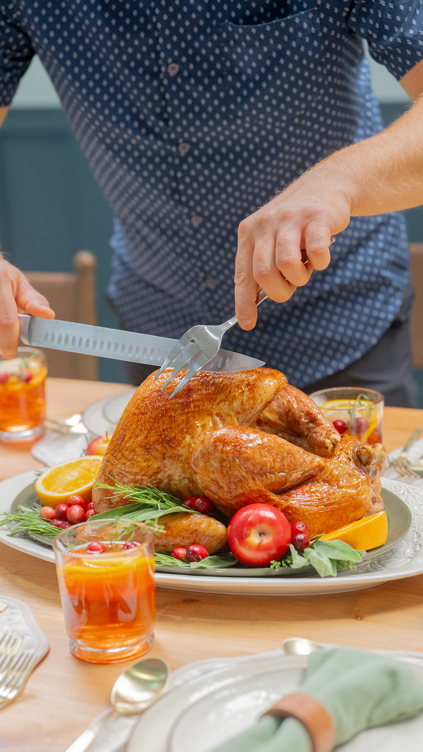 Carving the roast turkey at a set holiday table, with cranberries, orange slices and glasses of punch around the platter.