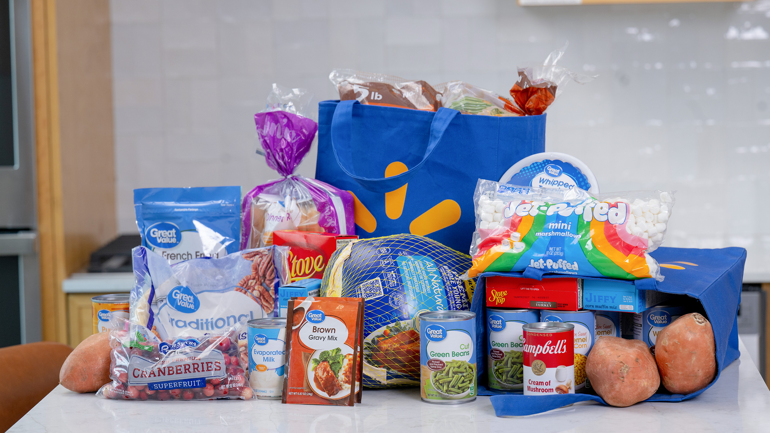 The complete 2026 Walmart Holiday Meal Basket arranged around a Walmart tote: a Butterball turkey, cans of green beans and corn, Campbell's Cream of Mushroom soup, Stove Top stuffing, JIFFY corn muffin mix, Jet-Puffed mini marshmallows, cranberries, sweet potatoes and dinner rolls.