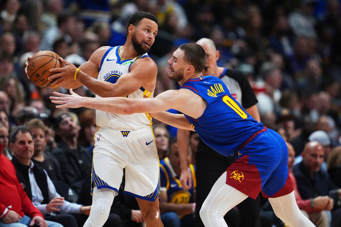 Stephen Curry in the white Golden State Warriors jersey, ball in both hands, defended by Denver's Christian Braun in the blue Nuggets No. 0 jersey — Ball Arena, Monday, October 26, 2026