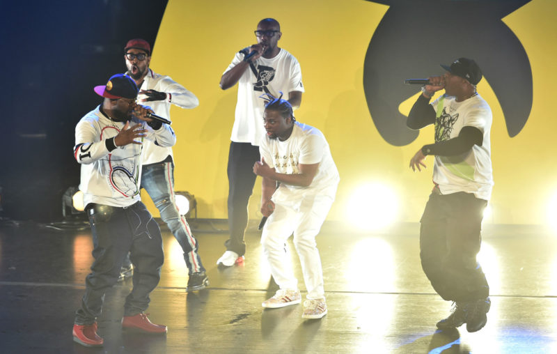 Wu-Tang Clan performing on stage in front of the group's signature yellow 'W' backdrop