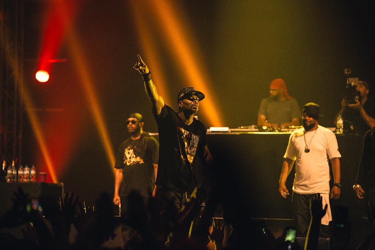 Wu-Tang Clan performing before a festival crowd under red and gold stage lights