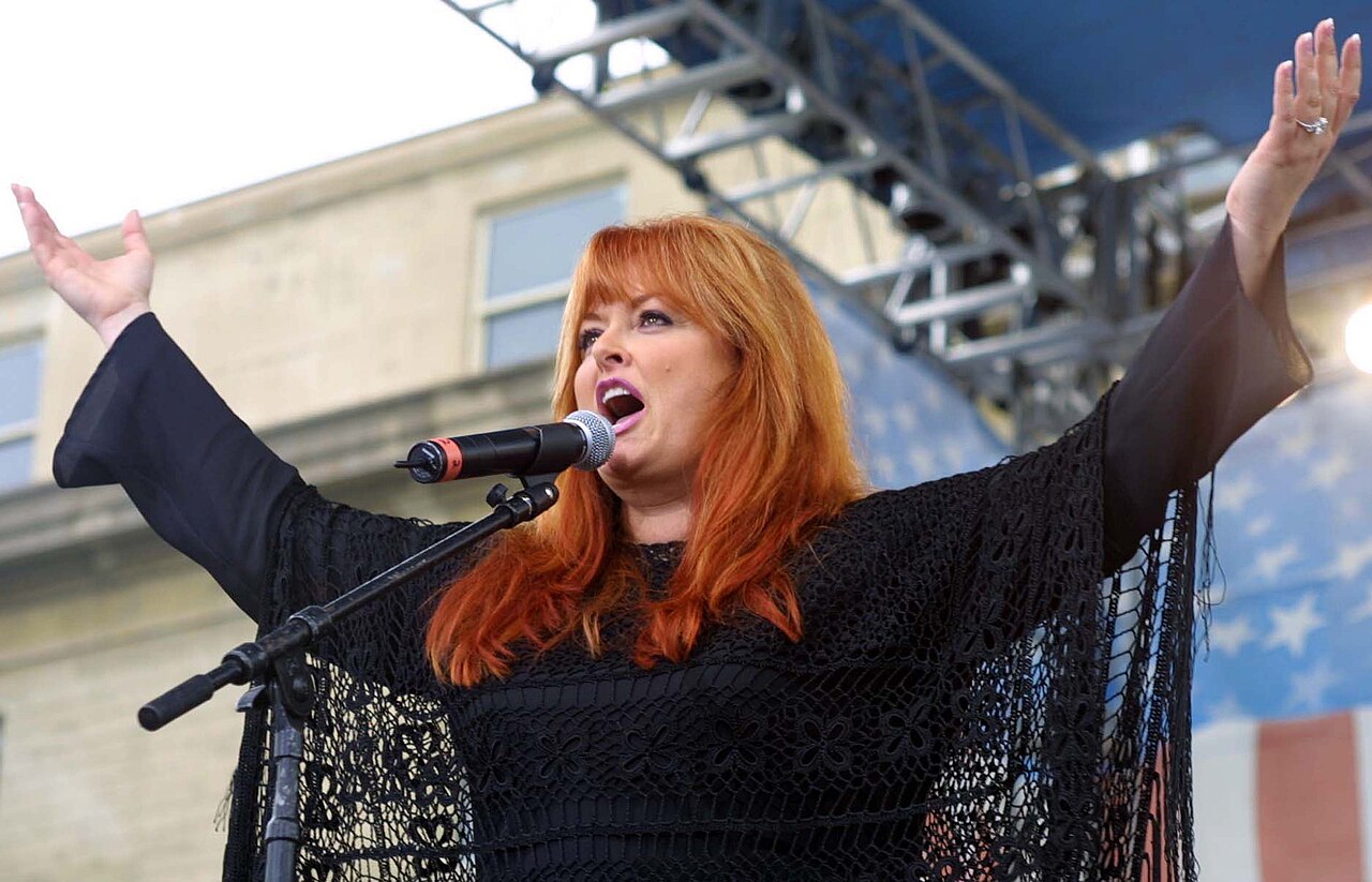 Wynonna Judd performing with open arms at a concert