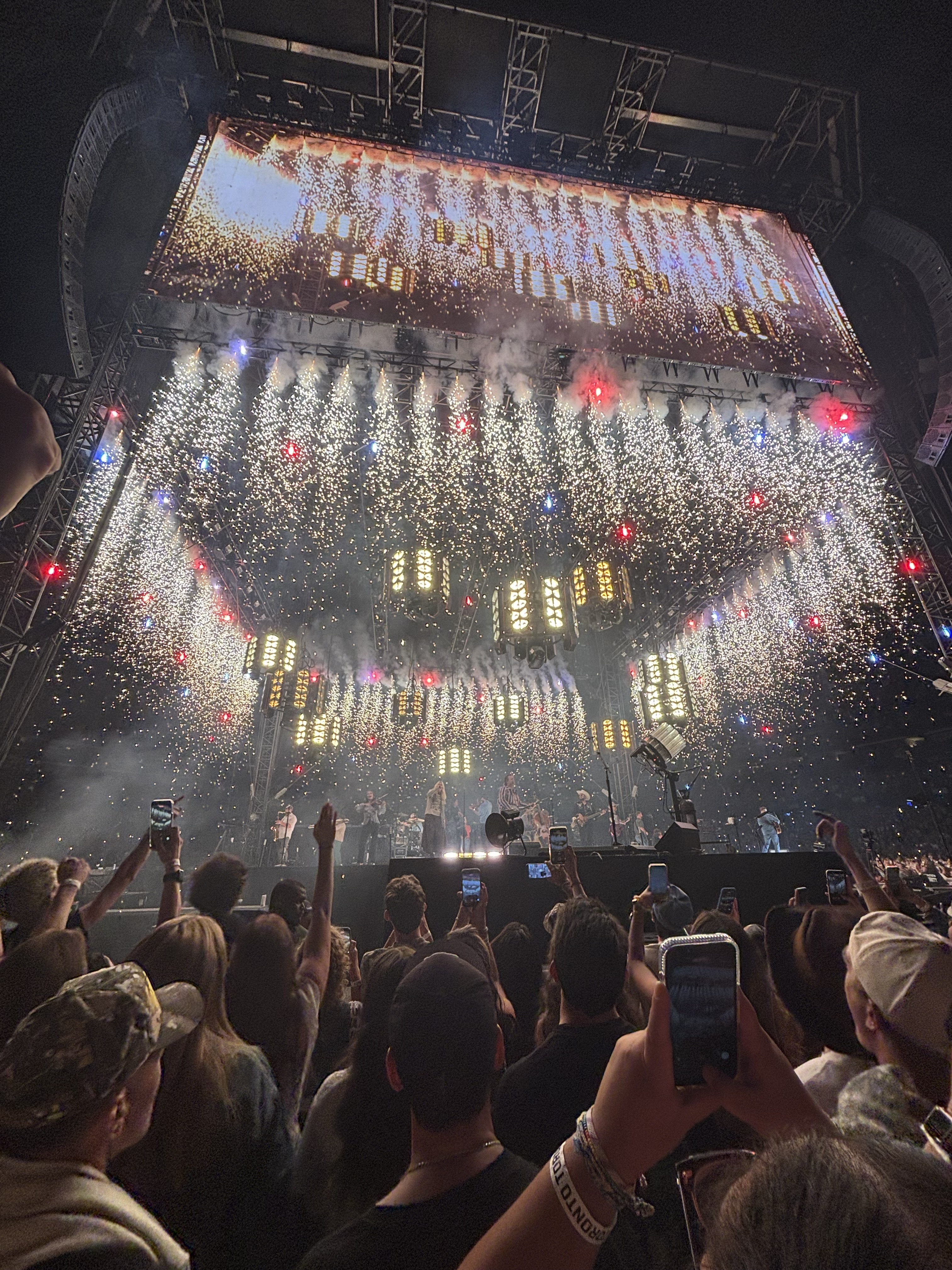 A stadium crowd watches pyrotechnics rain over the stage during the encore of Zach Bryan's 2026 With Heaven On Top Tour