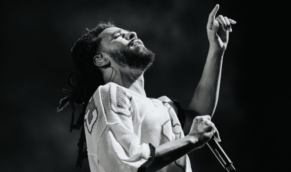 J. Cole performing live, arm raised, black and white